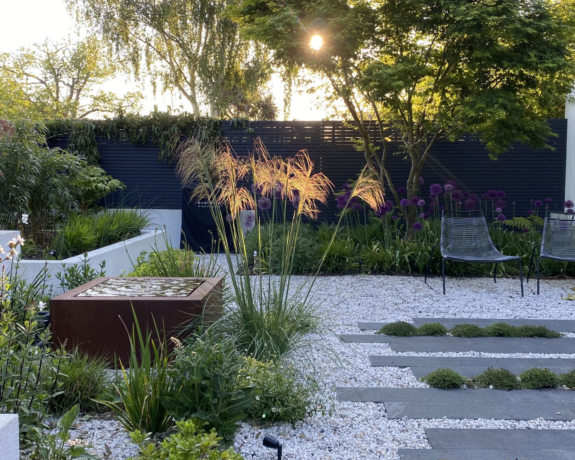 A real garden bed filled with small pea gravel surrounding drought-tolerant plants near a stone walkway