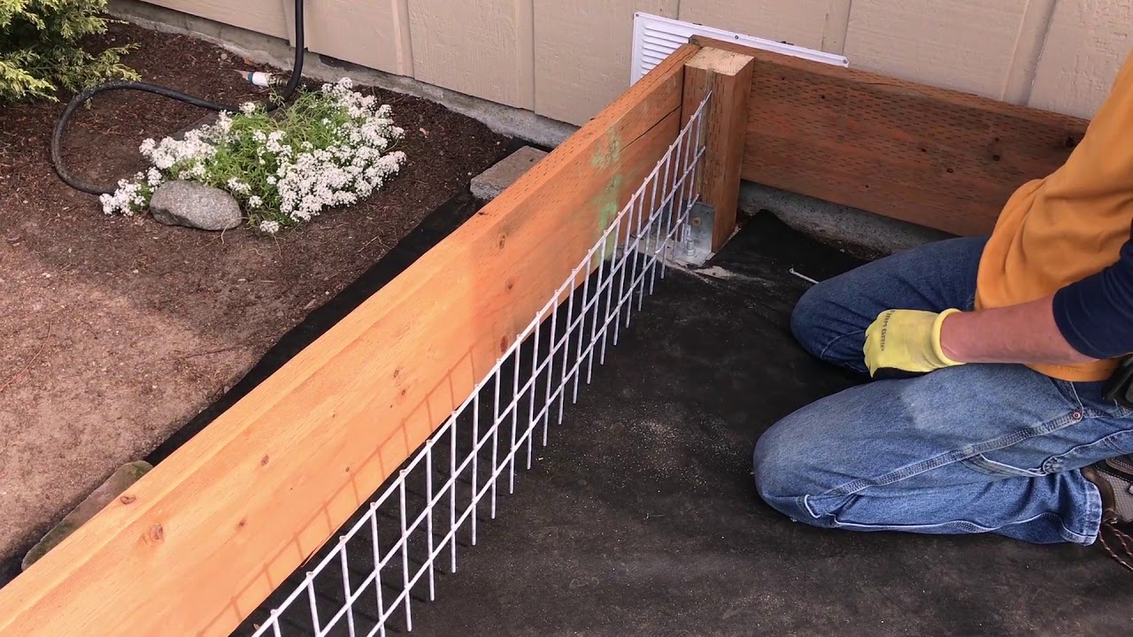 A person stapling galvanized hardware cloth along the bottom edge of a wooden deck to block animal entry, realistic home improvement photograph