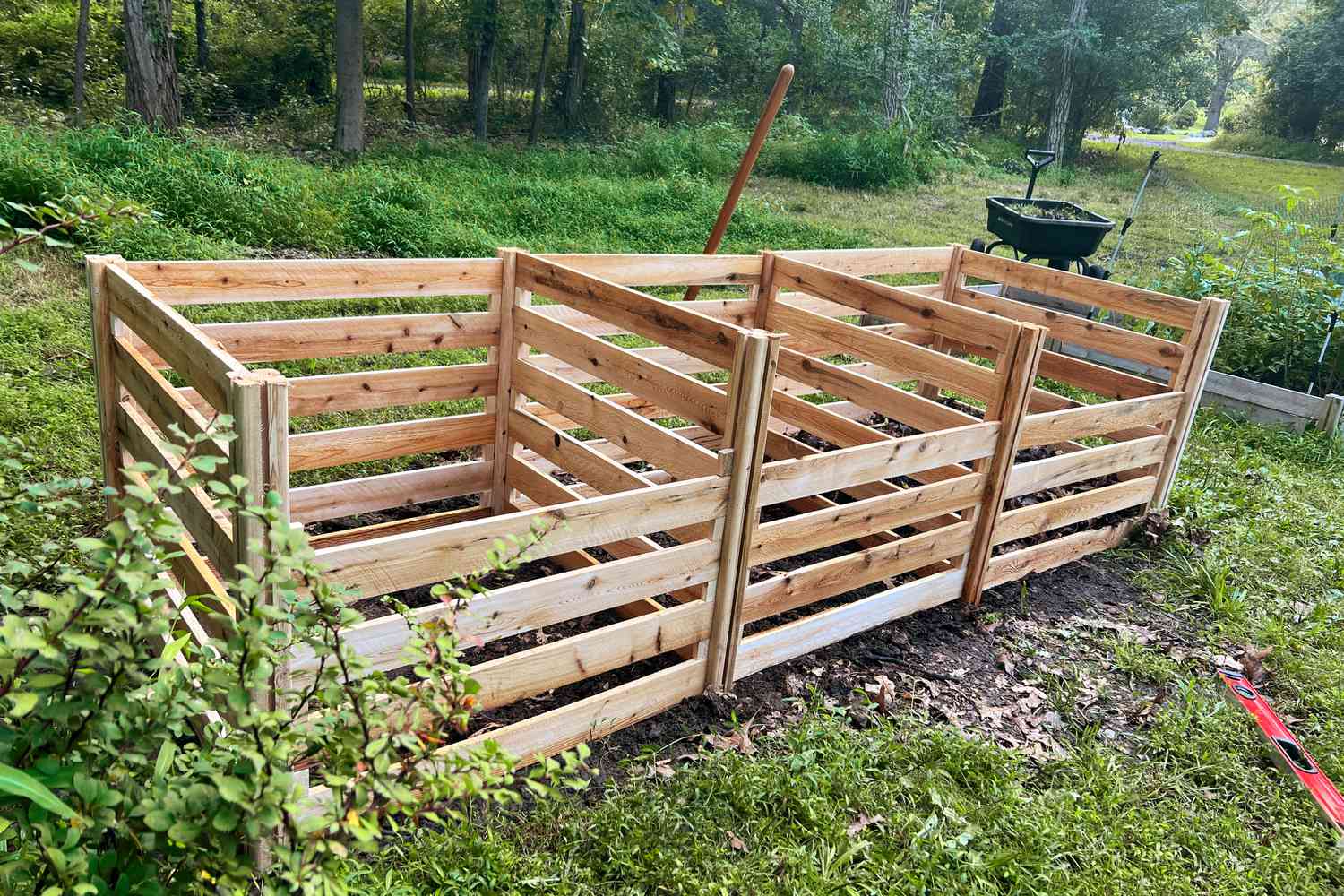 A real closed compost bin with a latched lid on a tidy backyard garden path, photographed in soft daylight