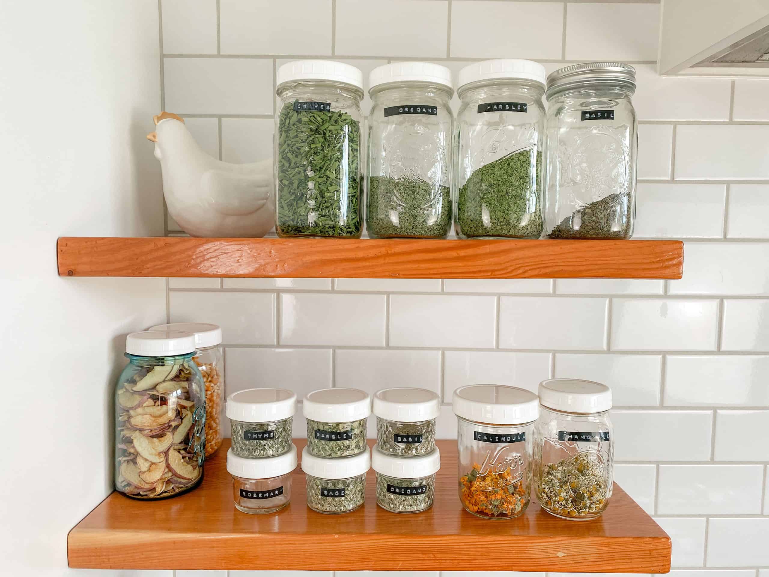 A small glass jar filled with dried oregano leaves on a kitchen counter with soft natural light